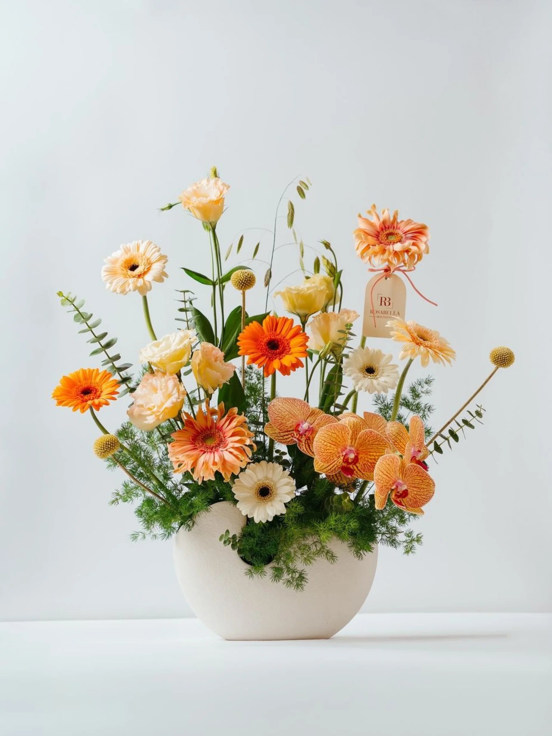 Golden Hour Blossoms arrangement with vibrant oranges and special orchids in a chic vase, available for flowers delivery to Dubai, Sharjah, and Muwaileh.