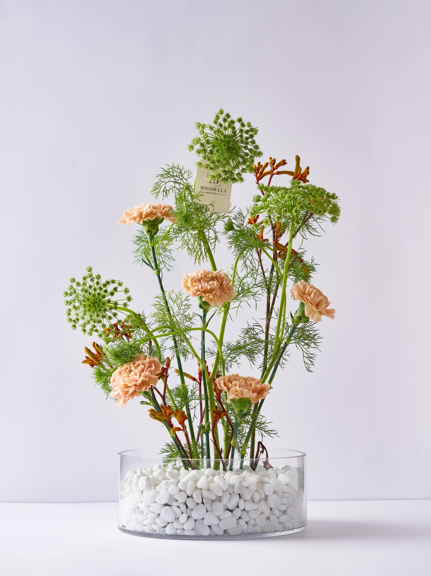 Natural Glow Vase Arrangement with soft peach blooms, lush greenery, and pebble accents in a clear vase, available at a flower shop in Dubai with delivery to Sharjah and Muwaileh.