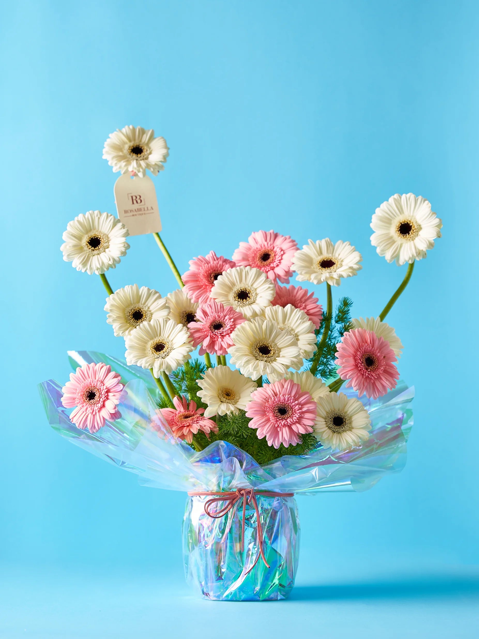 Rainbow Bliss Bouquet with pink and white blooms wrapped in iridescent rainbow packaging, available for flowers delivery to Dubai, Sharjah, and Muwaileh.