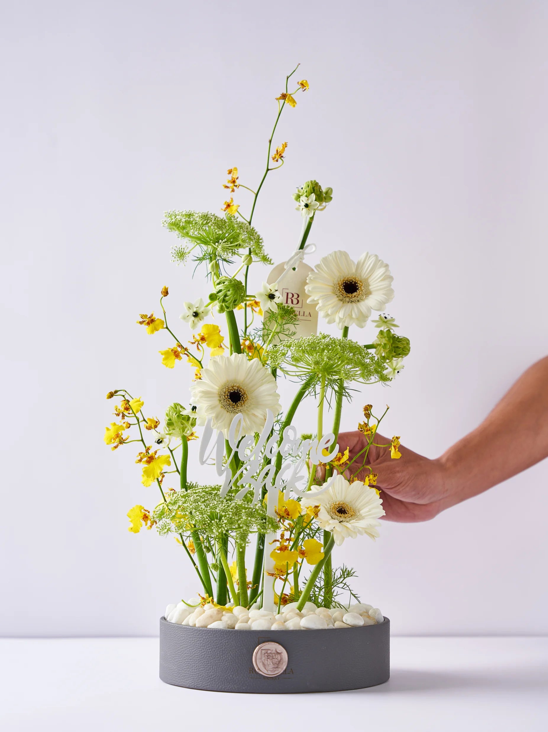 Sunlit Welcome Back arrangement with yellow blooms, fresh greens, and white flowers, accented with a "Welcome Back" message, available with flower delivery to Dubai and Sharjah.