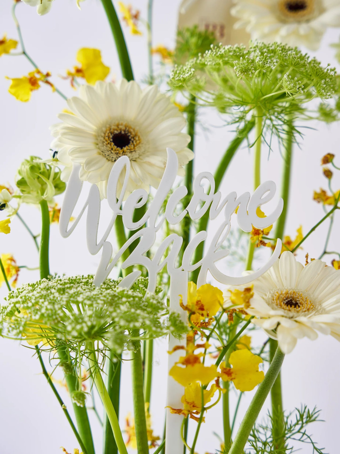 Sunlit Welcome Back arrangement with yellow blooms, fresh greens, and white flowers, accented with a "Welcome Back" message, available with flower delivery to Dubai and Sharjah.