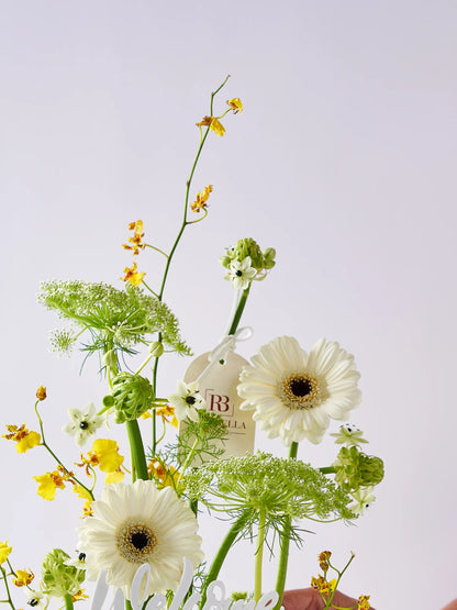 Sunlit Welcome Back arrangement with yellow blooms, fresh greens, and white flowers, accented with a "Welcome Back" message, available with flower delivery to Dubai and Sharjah.